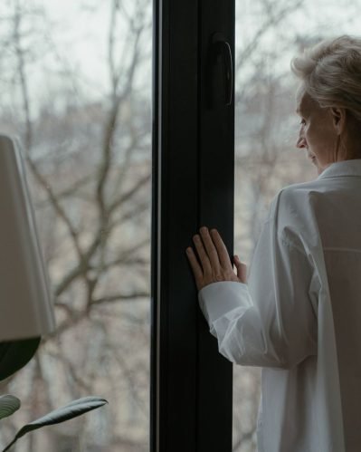 A senior woman in soft natural light at home — a quiet, reflective moment